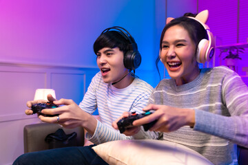 Young attractive asian woman playing video games at home neon lighted living room . Side view of a couple working in front of the same workstation.