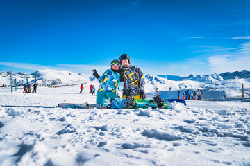 Couple, skier and snowboarder sitting on the snow and looking at camera, Pyrenees Mountains. Winter...