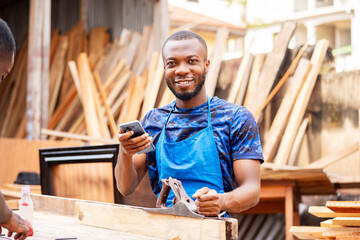 image of cheerful african man with a working tool and a smart phone- young black entrepreneur in a...
