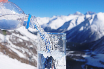Naklejka na ściany i meble Pouring water from bottle into a glass on a background of winter landscape of mountains. Healthcare hydration concept