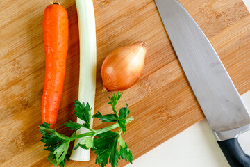 Mirepoix, onion, carrot, celery on a wooden cutting board with a knife. Vegetable mirepoix preparation. Horizontal top view landscape flat lay photo.