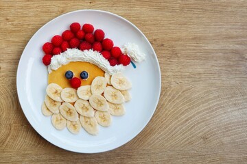 Santa claus pancake made it from pancake,bananas,blueberries,raspberries and whipped cream on plate...