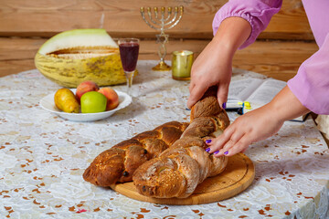 The hands of a Jewish woman break the challah during the Shabbat meal next to burning candles and a...