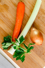 Onion, carrot, celery on a wooden cutting board with a knife for mirepoix. Mirepoix vegetable preparation. Portrait top view vertical flat lay photo.