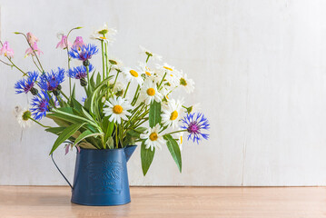 Bouquet of white daisies and blue cornflowers in blue vase on white wooden backgroud; copy space; Spring or summer greeting card