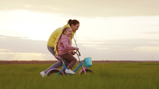 mother teaches ride bike little daughter child sunset. happy family. kid childhood dream learn how steer bicycle. daughter kid with mom operate two-wheeled children bike lawn summer autumn. family,