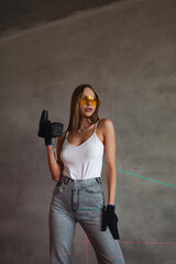 Beautiful blonde girl stands with construction tools in construction uniform in yellow glasses