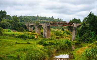 Fototapeta na wymiar Small railway bridge over small river near Manjakandriana, Madagascar, green grass and trees around. There is only small number of railroads on whole island