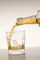 pour whiskey or bourbon into a glass on a beige white background vertical studio shot