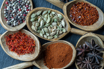 Set of spices in wooden spoons, closeup, top view. Various pepper, chili peppers, cardamom, carnation, star anise, paprika, and saffron for cooking