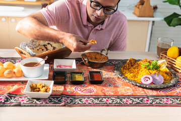 Indian men using hand to be picking up Indian food placed on the table, which is the culture of...