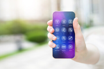 female hand shows a mobile phone with an astrological application with zodiac signs