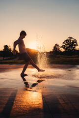 Boy playing in water fountain at a splash pad on summer evening © Cavan