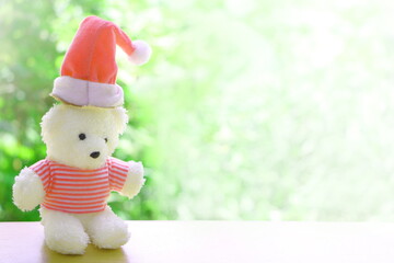 Close up one white teddy bear with red shirt and red Christmas cap on blur green and white background have copy space for put text
