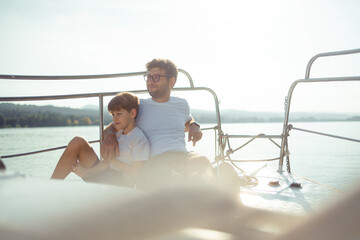 Father and son enjoying a day on the water. They sit on the bow of the ship and look into the distance