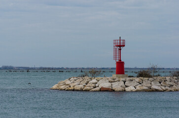 Un piccolo faro rosso lungo una massicciata del porto di Chioggia in una nuvolosa giornata invernale