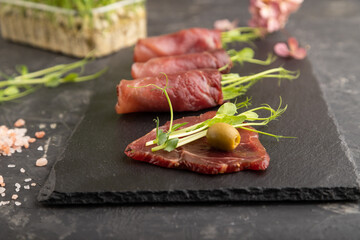 Slices of smoked salted meat with green pea microgreen on black. Side view, selective focus.
