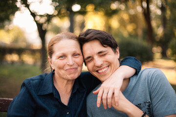 Happy mature mother hugging smiling adult son in park in summer