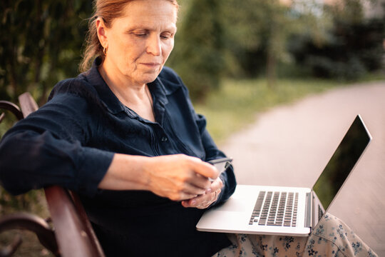 Mature business woman using smart phone and laptop computer in park