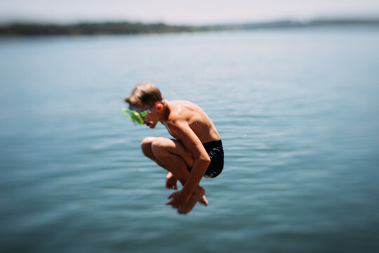 Young boy jumping into lake on summer day