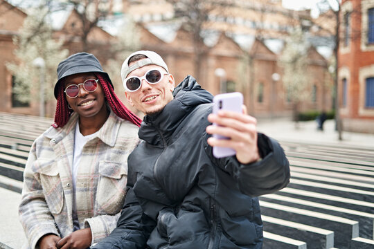 multiethnic couple using phone taking selfie, on the street