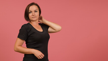 Obraz premium beautiful adult woman posing at the camera on a pink background in a black t-shirt