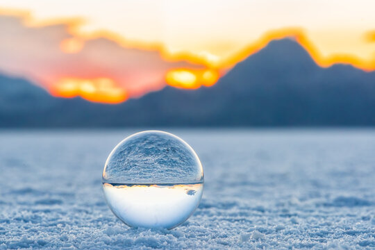 Crystal ball macro closeup ground level view of round glass globe with reflection of Bonneville salt flats and mountains at colorful sunset with orange and yellow colors
