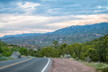 Sangre De Cristo mountains sunset on Bishops Lodge Road street in Santa Fe New Mexico with car driving, pink sunlight by Tesuque residential community