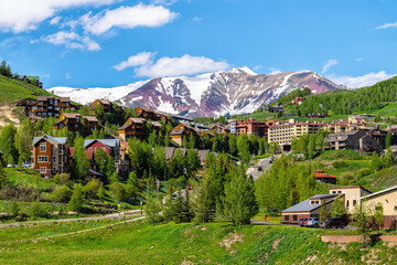 Fototapeta na wymiar Mount Crested Butte ski resort town village city in Colorado with houses on hill in summer and green trees by snow-capped mountains in background