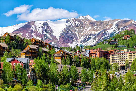Mount Crested Butte ski resort town, Colorado with houses homes, wooden lodge hotels on hill in summer and green trees by snow-capped mountains in background