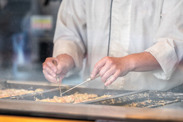 Closeup of man chef person cooking turning flipping over takoyaki Japanese octopus balls street food with steel turners at Ginza, Tokyo Japan