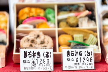 Closeup of traditional kaiseki bento box, lunchbox with price tag label in Japanese specifying price, ingredients and product description on retail store display in Tokyo, Japan - obrazy, fototapety, plakaty