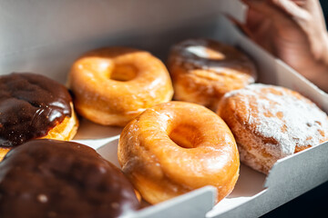 Man holding half a dozen of donuts doughnuts in carboard container box, glazed deep fried dessert pastry of Boston cream, chocolate filling - obrazy, fototapety, plakaty