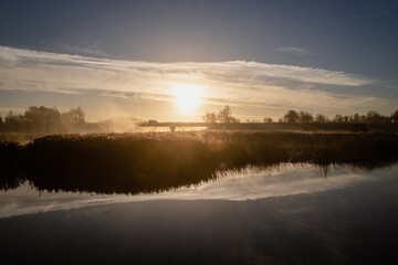 Fototapeta na wymiar morning mist covers river and bridge at sunrise, symmetric reflection of clouds