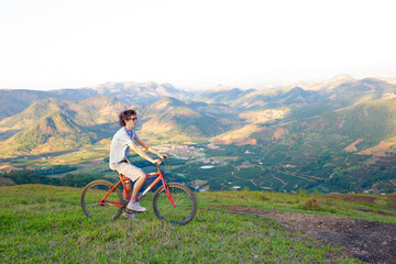 Young man riding a bicycle high on a mountain with a valley and mountains in the background.