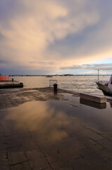 Le nuvole al tramonto si riflettono in una pozzanghera di pioggia sul selciato di Venezia