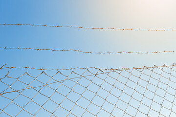 Barbed wire and fence on blue sky background at sunny day. The concept of hope and good days behind captivity.