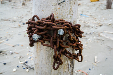 Una catena arrugginita legata attorno a un palo di legno sulla spiaggia - obrazy, fototapety, plakaty
