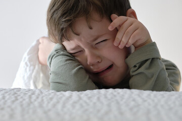 Cute young  boy crying near the bed
