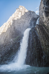 A high noisy and cold waterfall breaks out of a rocky gorge in the mountains in autumn, on a sunny autumn day