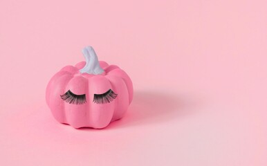 Halloween pink pumpkin with makeup, false eyelashes on the pink background, close-up
