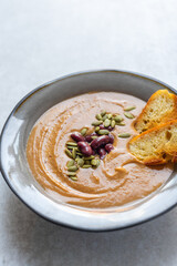 Healthy vegan pumpkin soup with red beans, pumpkin seeds, coconut cream and slices of fried bread