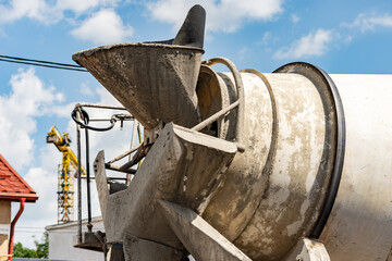 Close up to a concrete mixer truck loader with a yellow construction crane behind