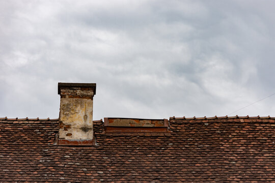 Old and weathered roof and chimney of a rustic home against a cloudy sky