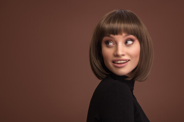 Portrait of a beautiful smiling brunette girl with a short haircut. Brown background. - 542486464