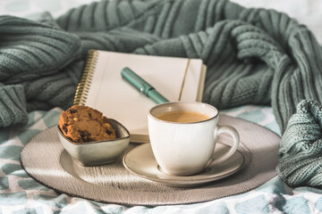Cup of coffee and cookie on cozy bed. Warm wool sweater for a cozy autumn weekend, breakfast in bed, coffee break. Hygge concept.