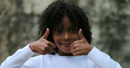 Cute black child giving thumbs up, Brazilian hispanic kid positive signal