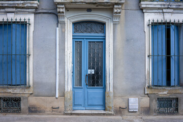 Fototapeta na wymiar Front view of a facade of a traditional house in an old town of Carcassonne France. Blue shutters and wooden door. In front of it a sidewalk without people