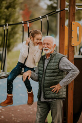 Grandfather spending time with his granddaughter in park playground on autumn day