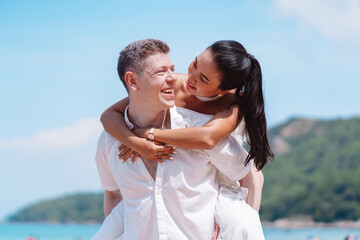 Young couple in love outdoor. Happy man giving piggyback ride to his woman and laughing at tropical...